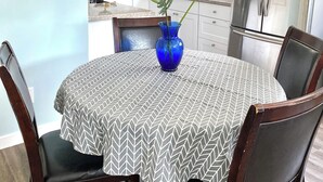 Un comedor con una mesa redonda cubierta por un mantel estampado, rodeada de sillas de madera. Un florero azul con una planta está sobre la mesa.