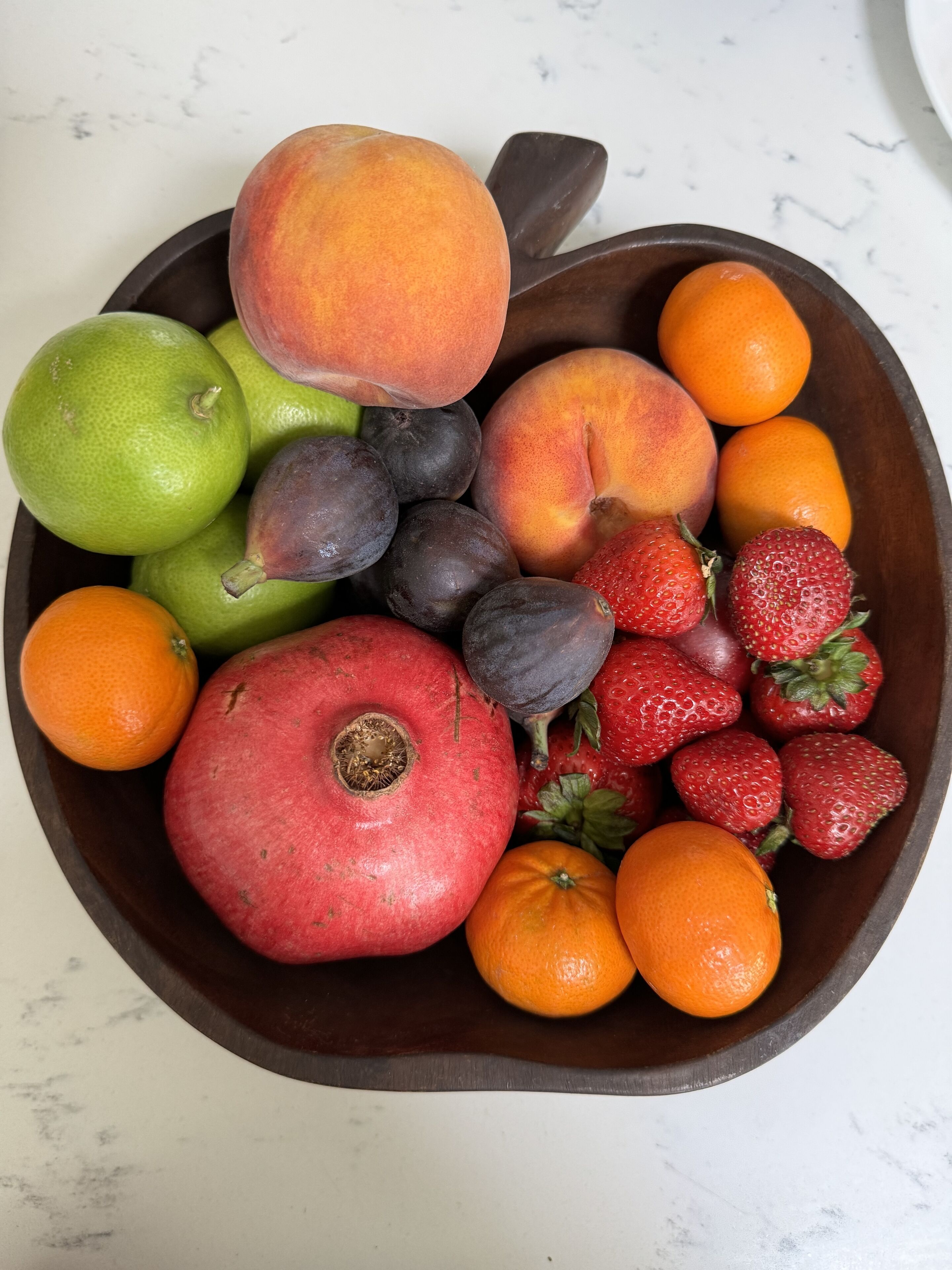 Un saladier en bois contenant divers fruits, notamment des pommes, des pêches, des prunes, des fraises et des oranges.