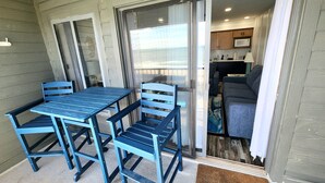 A patio with a table and chairs, a sliding glass door leading to a kitchen area with a sofa and a coffee table.