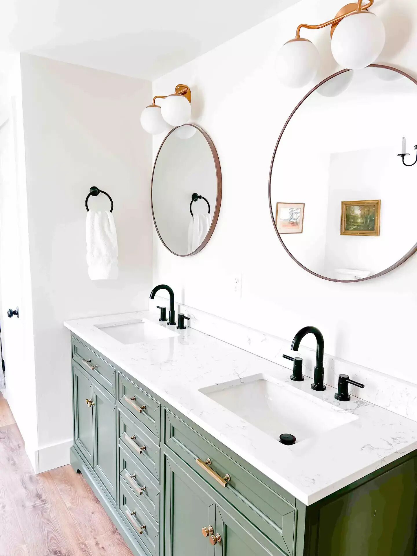 Un bagno con due lavabi, mobili verdi e specchi a parete con lampade sferiche.
