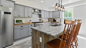 A modern kitchen with grey cabinets, a central island, and wooden chairs. - The Blueberry House - Spacious, Family & Pet-Friendly Retreat near Sebago Lake (Sebago)