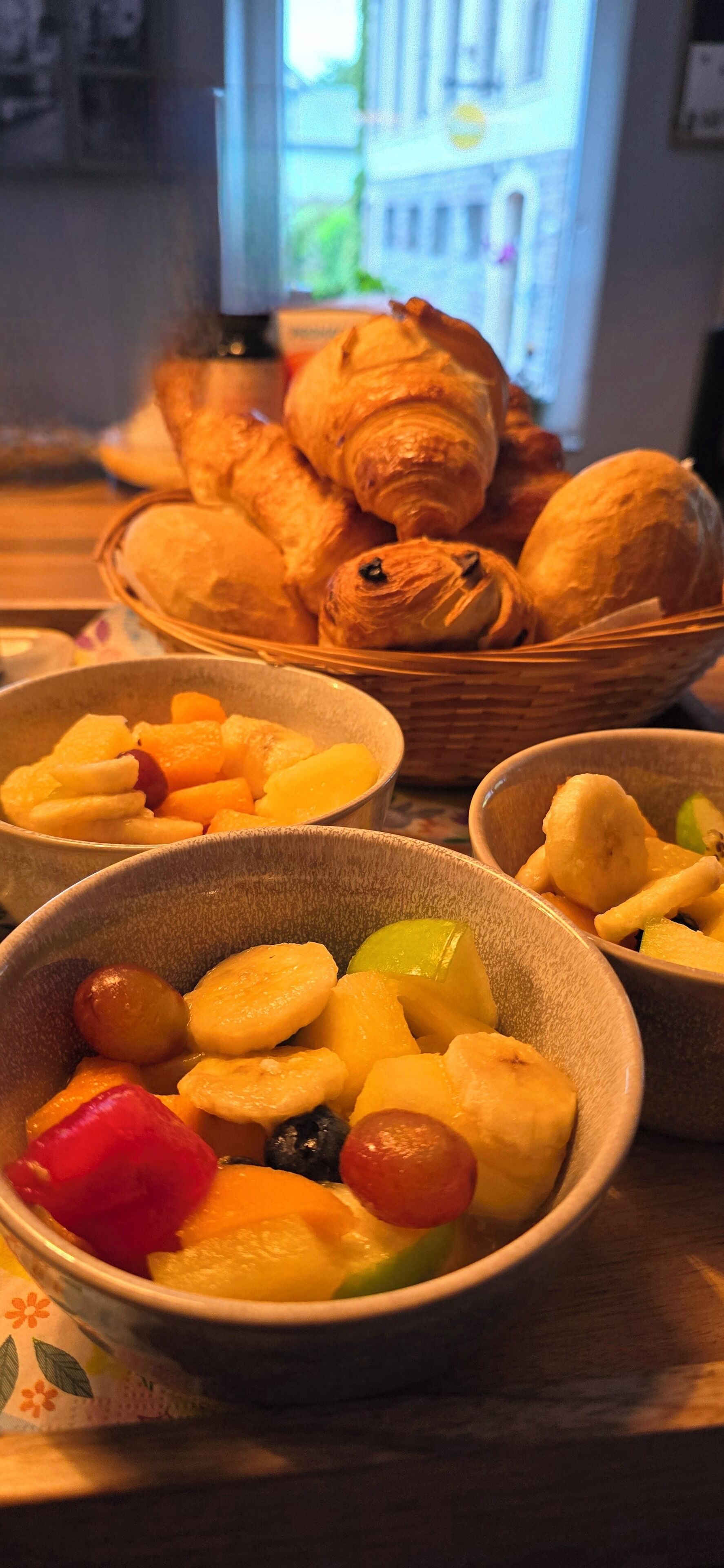 A table with bowls of fruit and a basket of croissants.