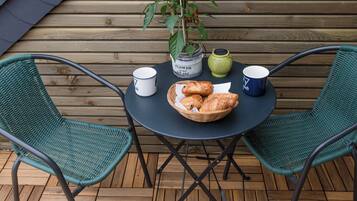 Una mesa redonda con un cesto de croissants, dos tazas, una maceta y una silla verde.