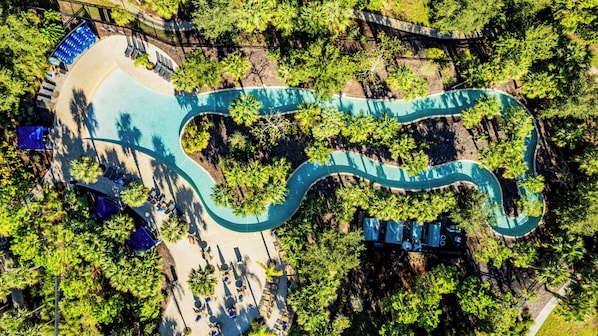 Vista aérea de un complejo turístico con una piscina serpenteante, zonas de descanso y abundante vegetación.