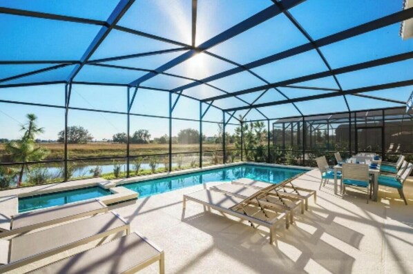 A covered outdoor swimming pool with lounge chairs and a view of the surrounding landscape. - Sunshine at Solterra (Davenport)