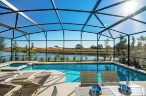 A pool with clear blue water, surrounded by lounge chairs and a view of a lake and hills. - Sunshine at Solterra (Davenport)