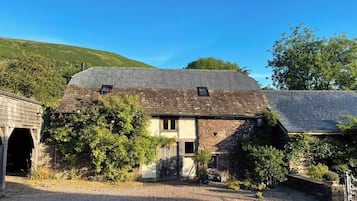 A stone building with a sloped roof, a gravel driveway, and surrounding greenery.