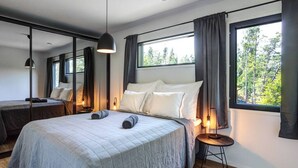 A modern bedroom with a large bed, bedside lamps, and a view of trees through the window. - Villa Syreeni - Seafront/Jacuzzi (Porvoo)