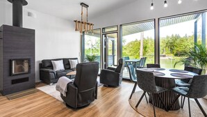 A modern living room with a fireplace, black leather furniture, and large windows offering a view of greenery. - Villa Syreeni - Seafront/Jacuzzi (Porvoo)