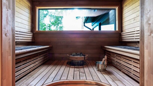A sauna with wooden benches, a window, and a metal container with a handle. - Villa Syreeni - Seafront/Jacuzzi (Porvoo)