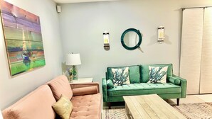 Uma sala de estar com um sofá verde, um sofá rosa, uma mesa de centro de madeira e um tapete colorido com padrão.