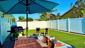 Um pátio com mesa, cadeiras, churrasqueira e um grande guarda-sol.