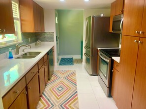 A kitchen with wooden cabinets, stainless steel appliances, a sink, and a patterned rug.