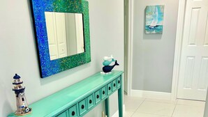 Um aparador azul-esverdeado com objetos decorativos, um tapete estampado e um espelho com moldura de mosaico.
