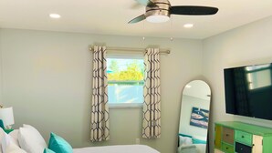 Quarto com cama, travesseiros, televisão, penteadeira e ventoinha no teto.