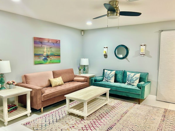 A living room with two sofas, a coffee table, a ceiling fan, wall art, and a patterned rug.