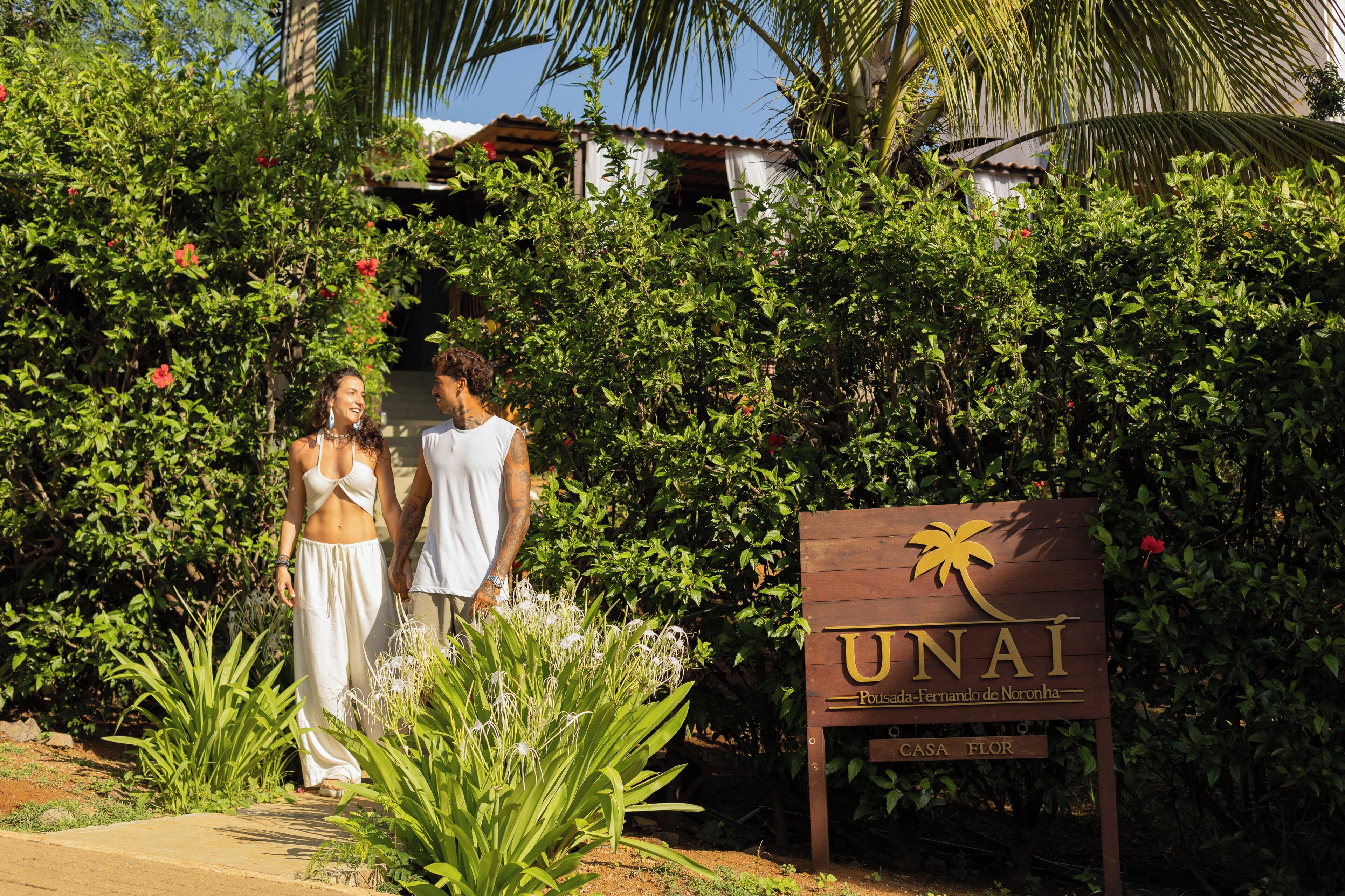 A sign for 'UNAI' with a palm tree logo, surrounded by lush greenery and plants.