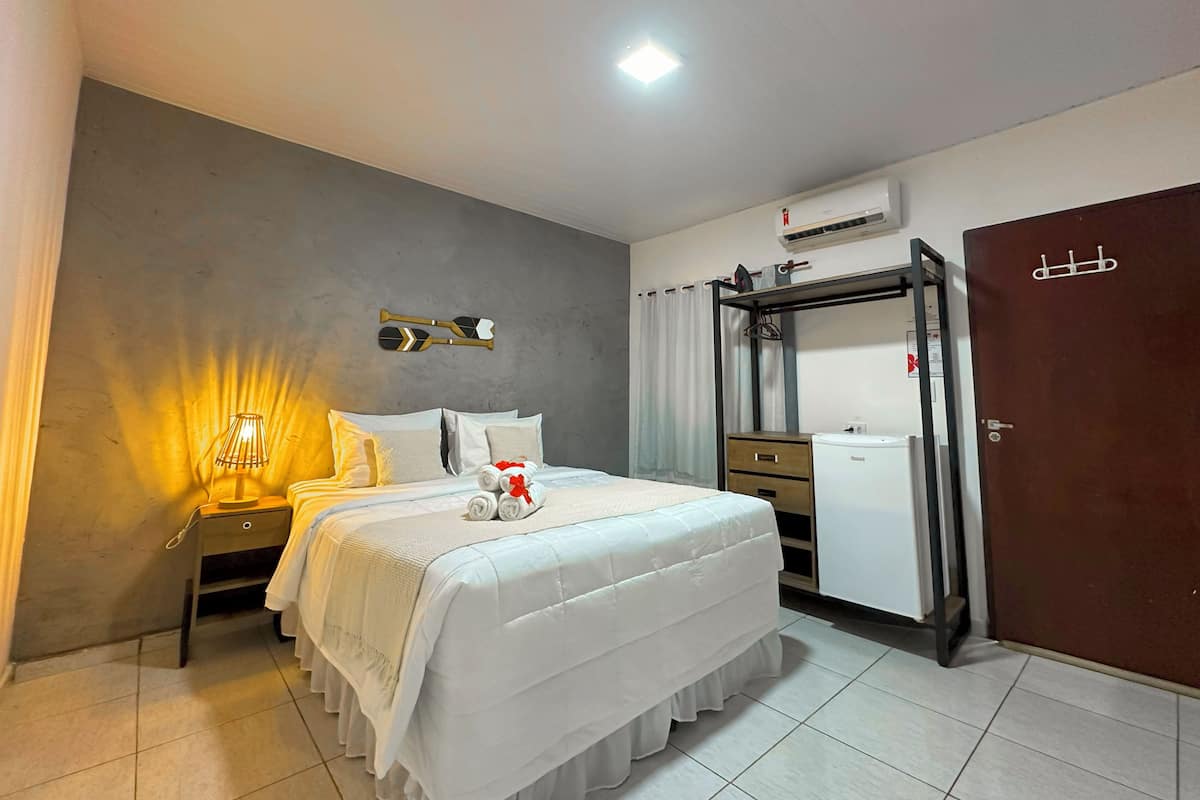 A hotel room with a bed, a nightstand, a mirror, a wardrobe, and an air conditioning unit.