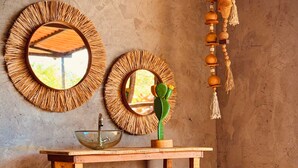 Quarto rústico com mesa consola de madeira, duas molduras redondas, um cacto, uma tigela, um vaso e uma cesta trançada.