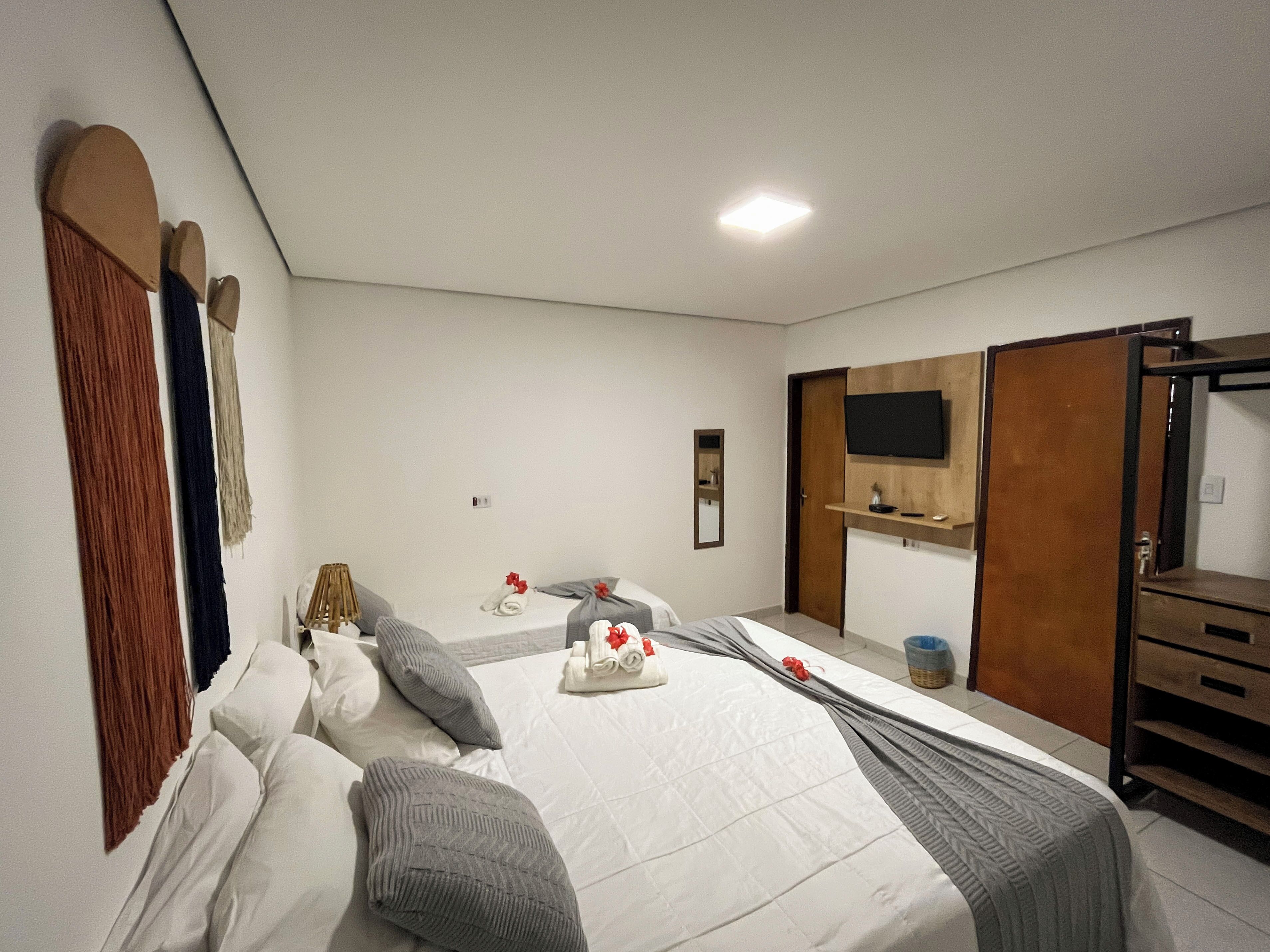 A hotel room with a bed, a TV, a mirror, and a wooden wardrobe.