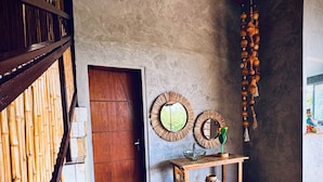 Um quarto com porta de madeira, uma pequena mesa de madeira com uma tigela e um vaso, e uma parede com dois espelhos redondos.