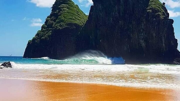 Uma praia com uma formação rochosa imponente ao fundo.