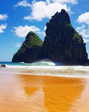 Una playa con una formación rocosa destacada al fondo.