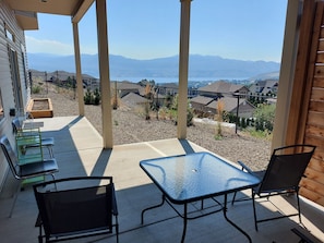 A covered patio with a table and chairs, a wooden bench, and a view of a residential area with houses and mountains in the background.