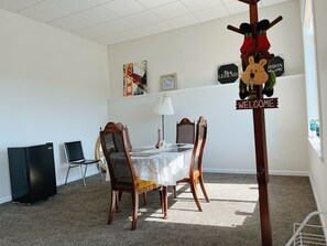 A dining area with a table set for four, surrounded by wooden chairs. There is a 'Welcome' sign, a 'Fashion' sign, and a 'Be a Legend' sign on the wall.