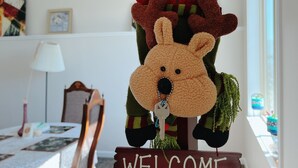 Ein weiches Rentier hängt an einem 'WELCOME'-Schild in einem Zimmer mit Essbereich.