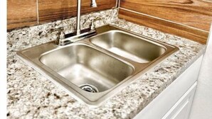 A kitchen with a double stainless steel sink, granite countertop, and wooden backsplash. - “NEW” Traveler’s Getaway (Pinellas Park)