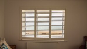 Un dormitorio con cama, ventana con persianas, radiador y vista a la playa.