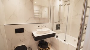 Un baño moderno con pared de mármol, inodoro negro, lavabo blanco y ducha con cerramiento de vidrio.