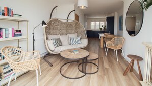 Una sala de estar acogedora con un sillón colgante, un sofá, una mesita redonda y una estantería.