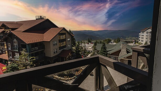 A multi-story building with a prominent roofline, a parking area, and a view of distant mountains. - HH 414 - Village/mountain views from this Charming Village studio! (Snowshoe)