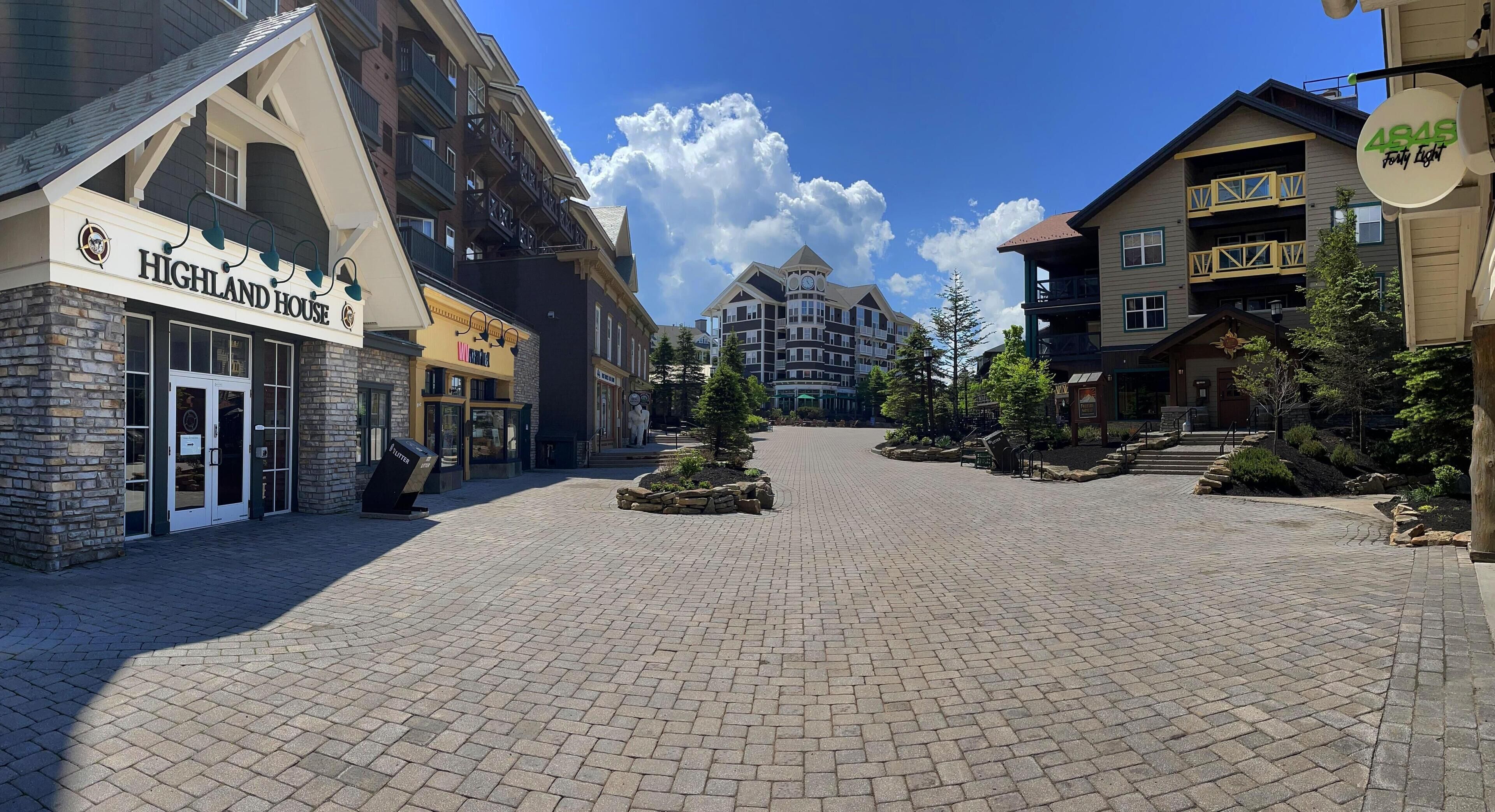 Un hotel con fachada de piedra, un letrero que dice "Highland House" y un patio empedrado con árboles y un elemento central.