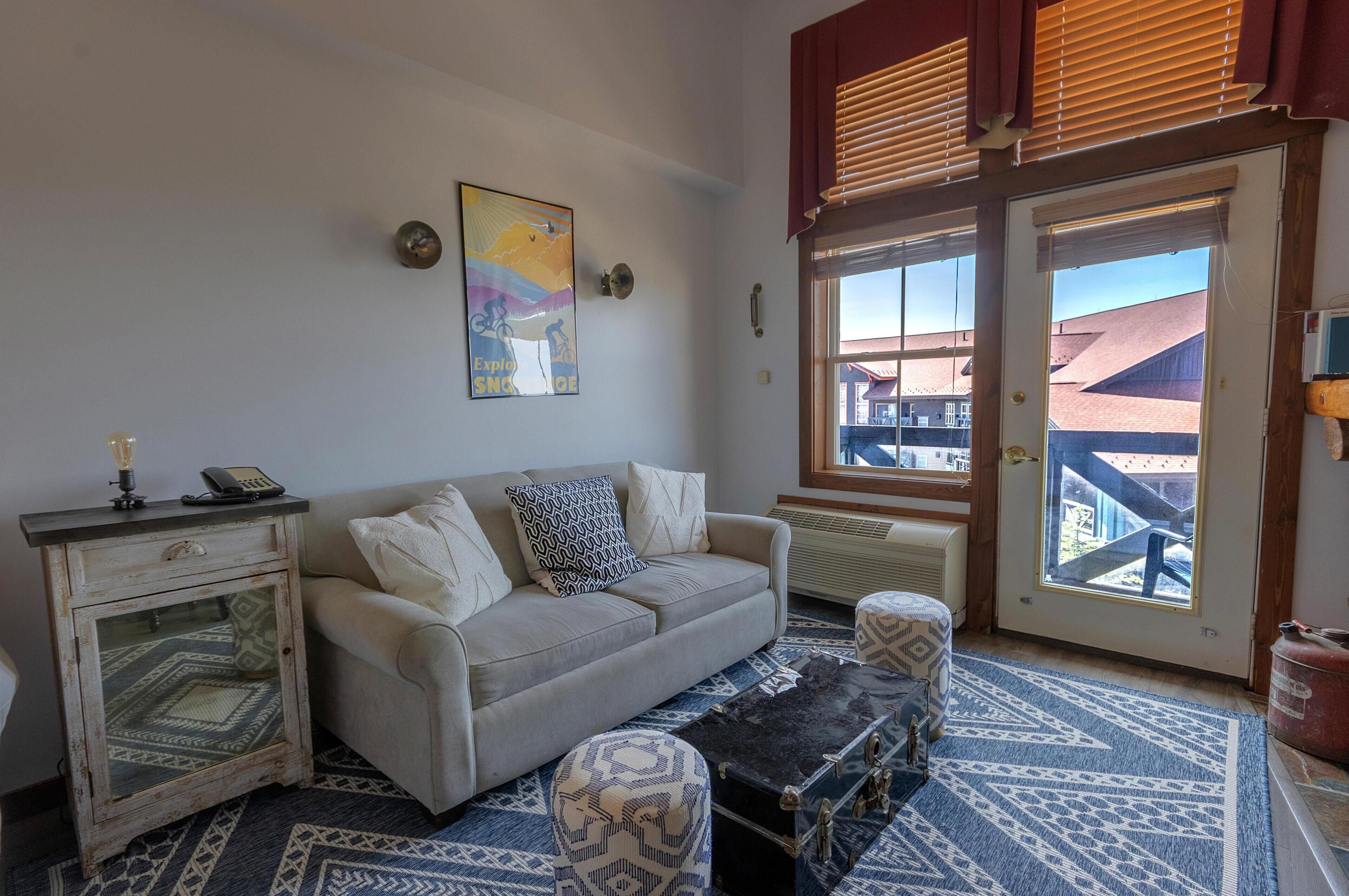 A cozy living room with a sofa, patterned ottoman, and a decorative lamp.