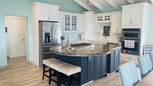 Une cuisine moderne dotée d’un îlot central, de meubles blancs, d’appareils électroménagers en acier inoxydable et d’un mur d’accent bleu clair.