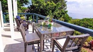 Une terrasse extérieure avec des meubles en osier, une table à plateau en verre et des plantes en pot.