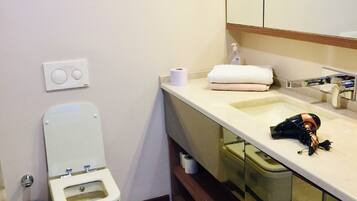 A bathroom with a toilet, sink, mirror, and a trash bin.