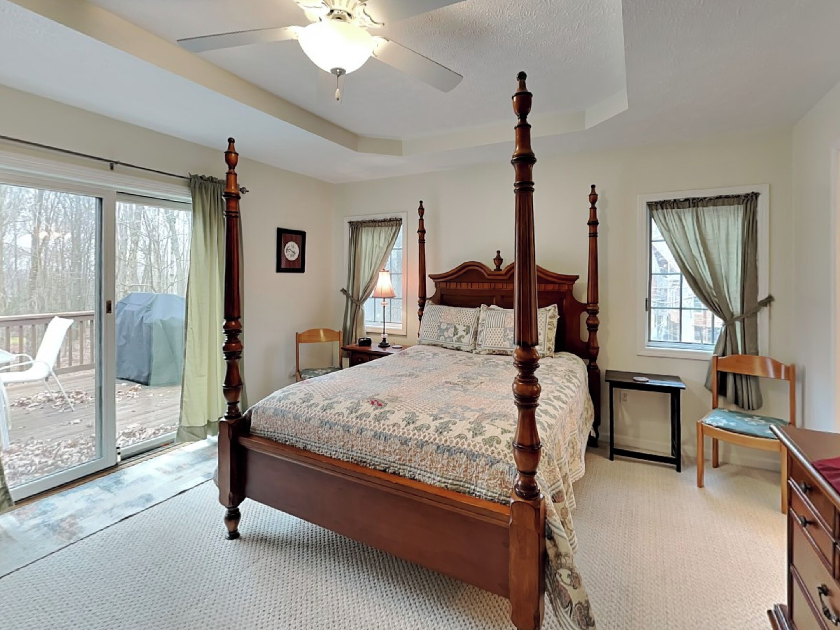 A bedroom with a four-poster bed, a ceiling fan, a desk, and a chair.
