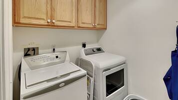 A laundry area with a front-loading washer and dryer, wooden cabinets above, and a laundry basket.