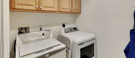 A laundry area with a front-loading washer and dryer, wooden cabinets above, and a laundry basket.