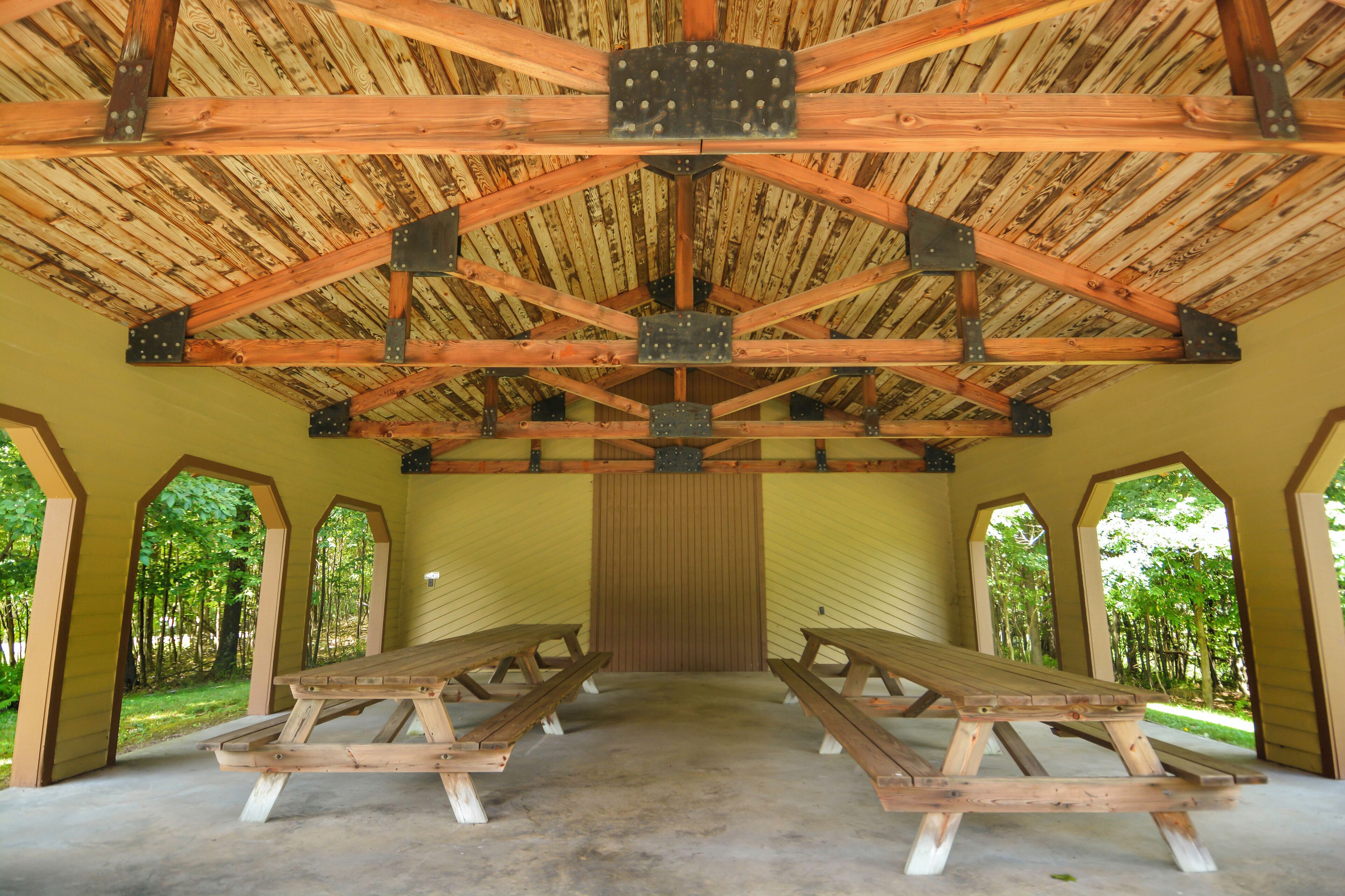 A covered picnic area with picnic tables and a wooden ceiling structure.