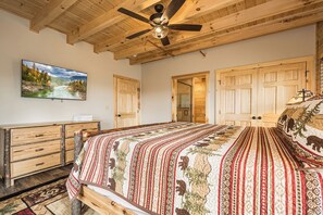 Une chambre avec un plafond en bois, un lit recouvert d’une couvre-lit à motifs, une commode et un tableau représentant un paysage.