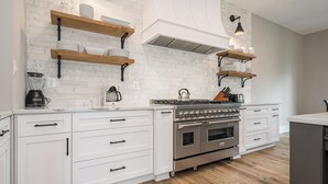 A modern kitchen with white cabinetry, a stainless steel stove, and wooden shelves. - Timber Ridge Haus by Taylor Made Deep Creek (McHenry)