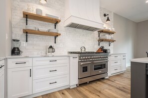 Una cocina moderna con armarios blancos, una estufa de acero inoxidable y repisas de madera.