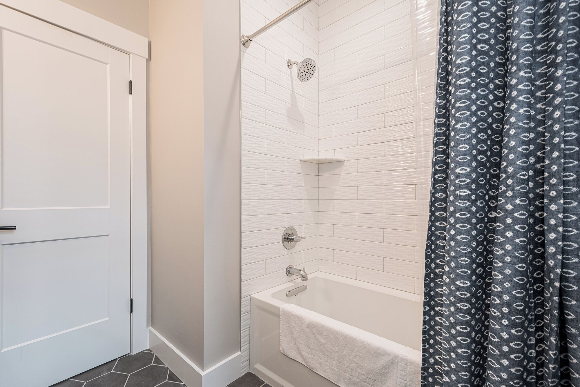 Une salle de bain avec une porte blanche, une douche avec un mur recouvert de carreaux blancs et une baignoire avec une serviette.