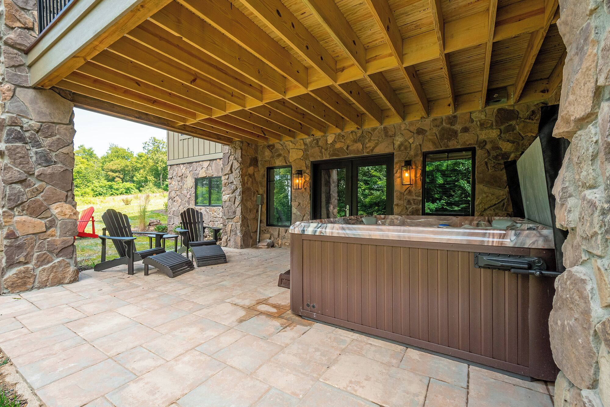 A stone exterior with a wooden pergola, a hot tub, and outdoor seating.