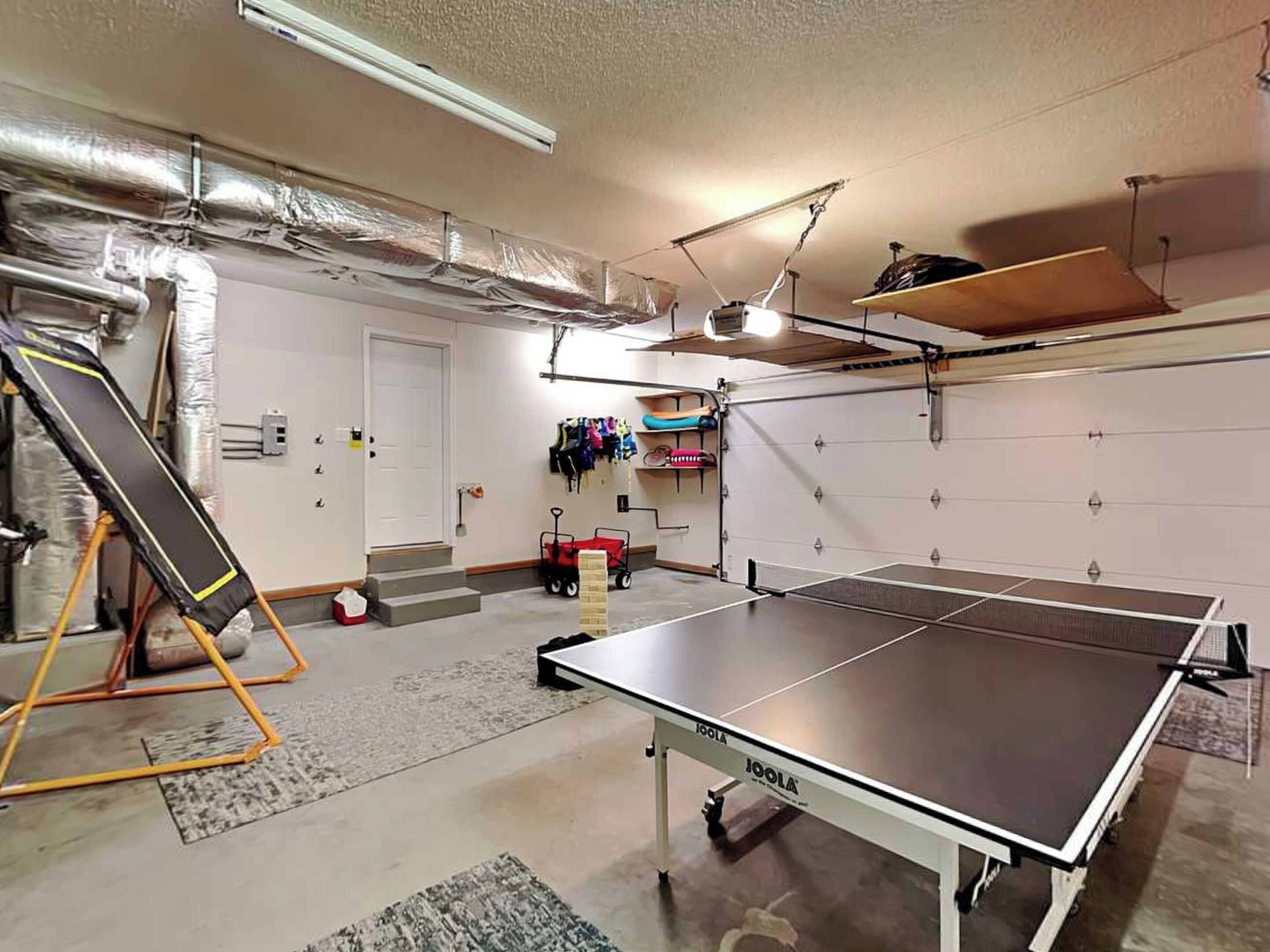 A spacious indoor area with a ping pong table, a trampoline, and a garage door.